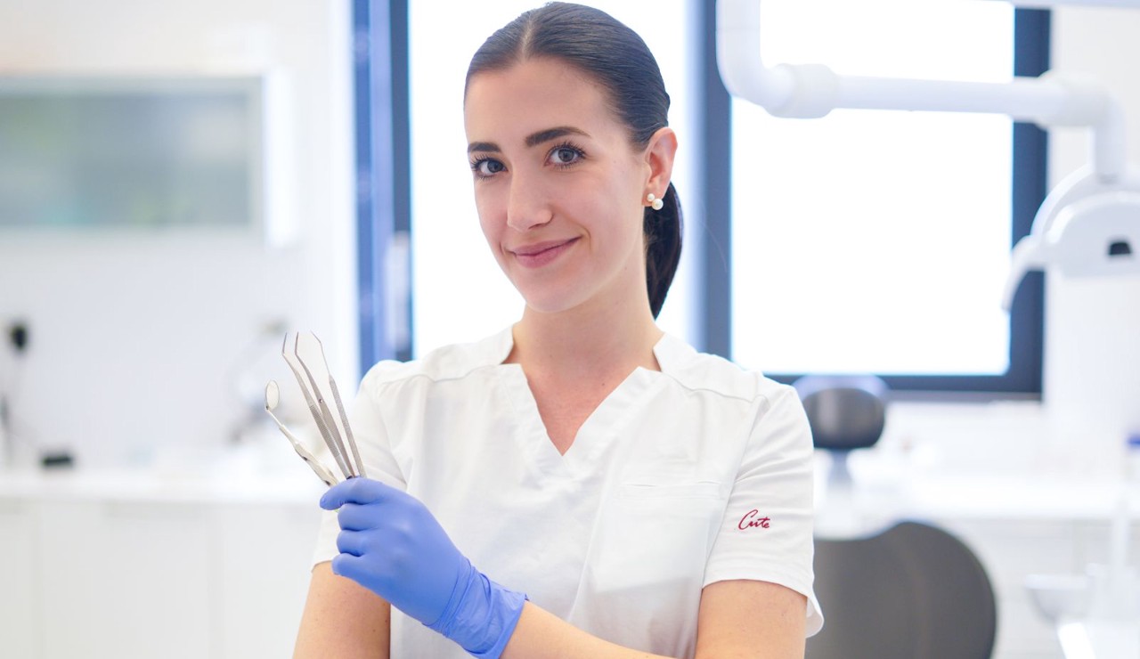 Doktorica s osmijehom drži dentalne instrumente u rukama i gleda prema kameri, spremna za početak pregleda.
