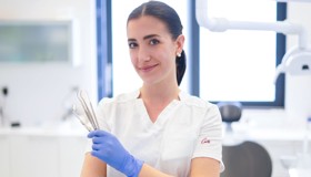 Doktorica s osmijehom drži dentalne instrumente u rukama i gleda prema kameri, spremna za početak pregleda.