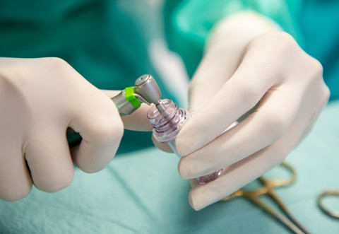 Ruke stomatologa u rukavicama dok precizno postavljaju dentalni implantat na kirurški alat tijekom zahvata.