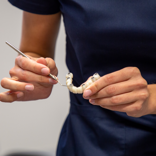 Doktorica drži u ruci model All-on-4 rješenja i pokazuje na njega, objašnjavajući princip fiksne protetske terapije na implantatima.