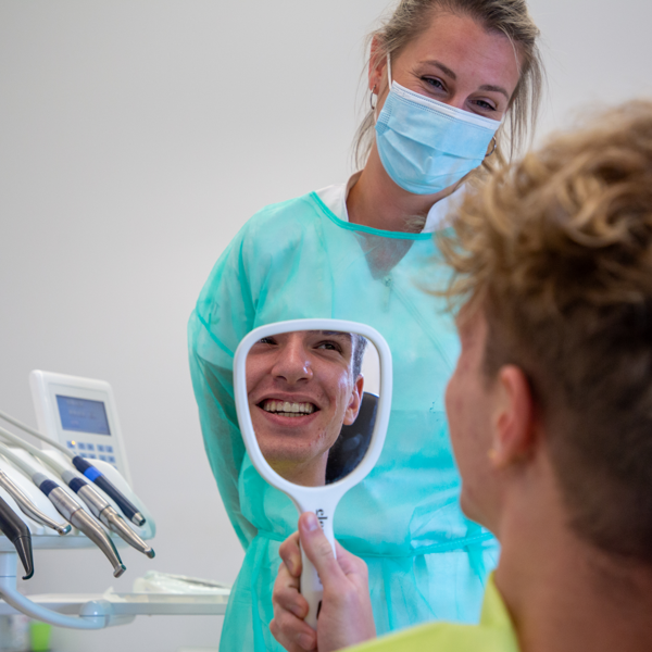 Pacijent s nevidljivim aparatićem promatra svoj osmijeh u ogledalu, provjeravajući izgled i diskretnost ortodontske terapije.