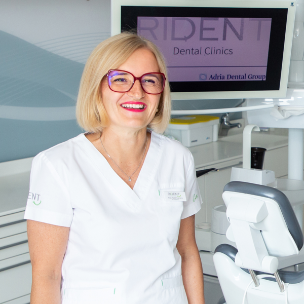 Doktorica u ordinaciji stoji s osmijehom na licu, stvarajući ugodnu i profesionalnu atmosferu u dentalnoj klinici.