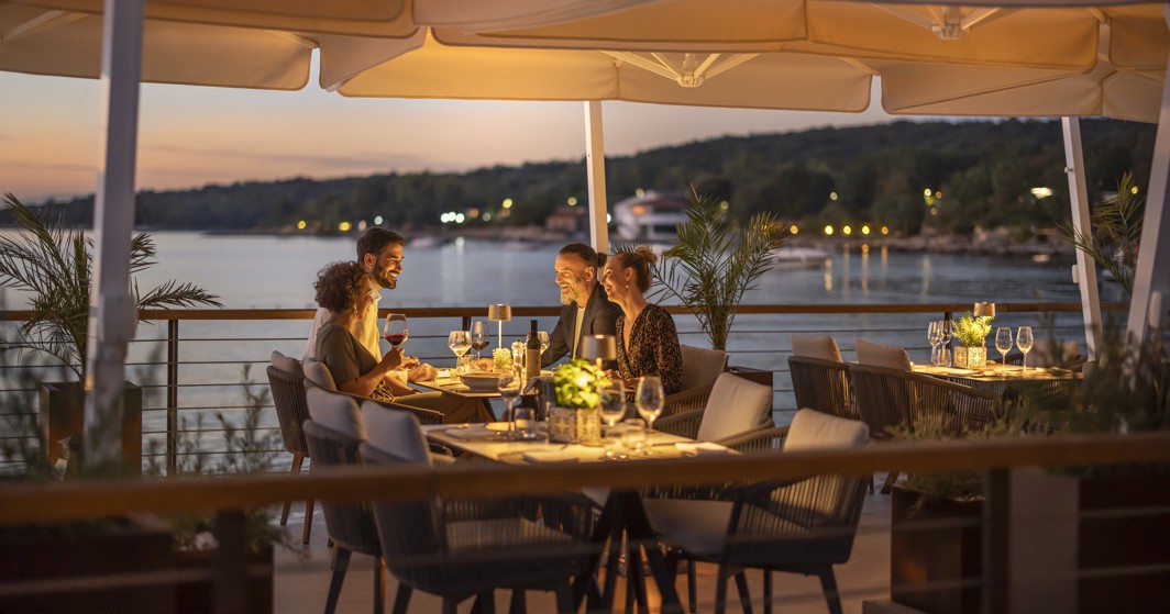 Group of friends enjoying a dinner at the 7 Seas restaurant & Bar near Aminess Style Camping Atea Resort, with a beautiful view of the sunset.