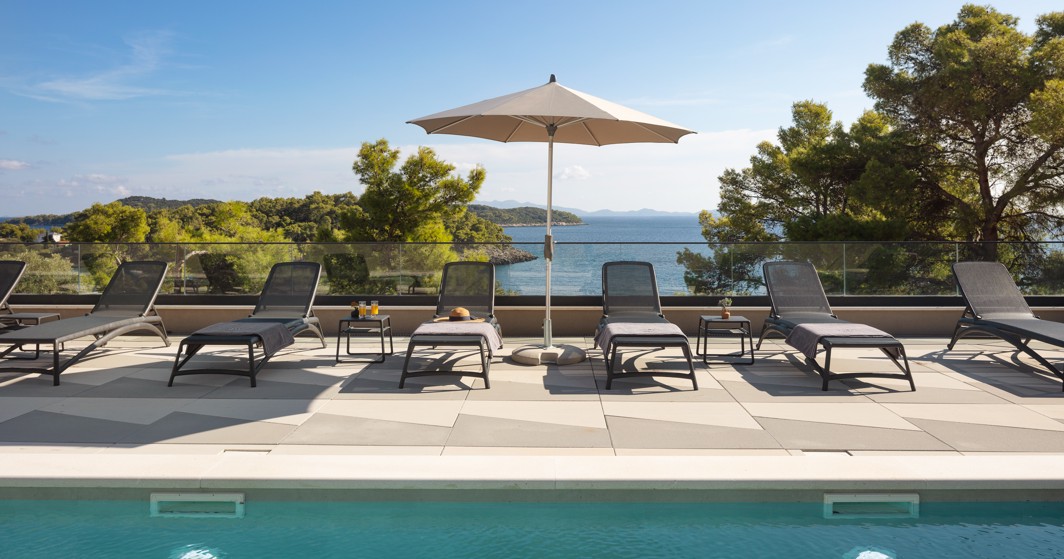 Buitenzwembad in Aminess Alfir Resort met ligbedden, parasols en uitzicht op zee in een ontspannen dagsfeer