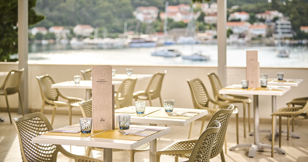 Miza, postavljena s krožniki, priborom in kozarci na terasi, s čudovitim pogledom na okolico v Aminess Vival Port9 Resort na Korčuli.