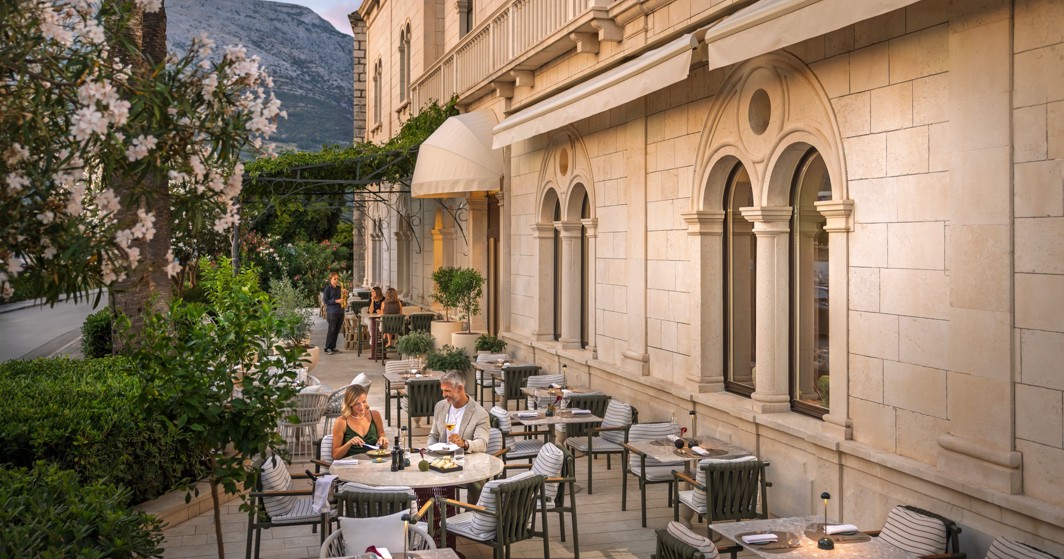 A couple dines on the terrace of Aminess Younique Korcula Heritage Hotel by the stone facade.