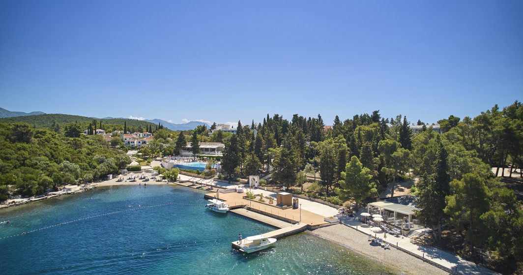 Ein Panoramablick auf die Bucht in der Nähe von Aminess Port9 Planet Camping Korcula, der das klare blaue Wasser, den mit Kiefern bewachsenen Ufer und einen Sandstrand hervorhebt, der ideal für Entspannung auf der Insel Korcula ist.