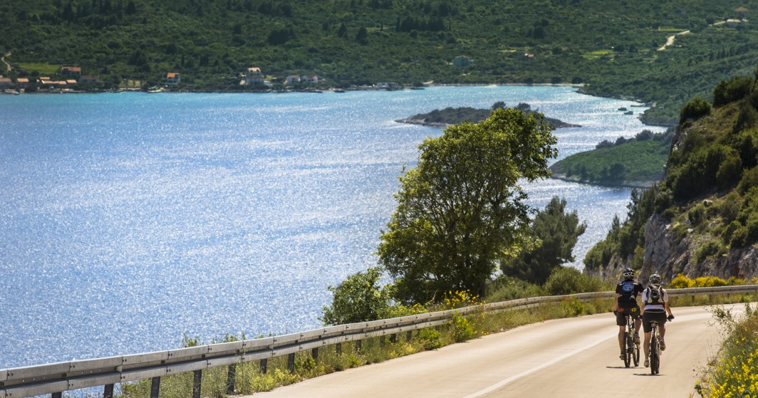 Cyclist riding along a peaceful road surrounded by nature and sea views near by Aminess Grand Azur Hotel.
