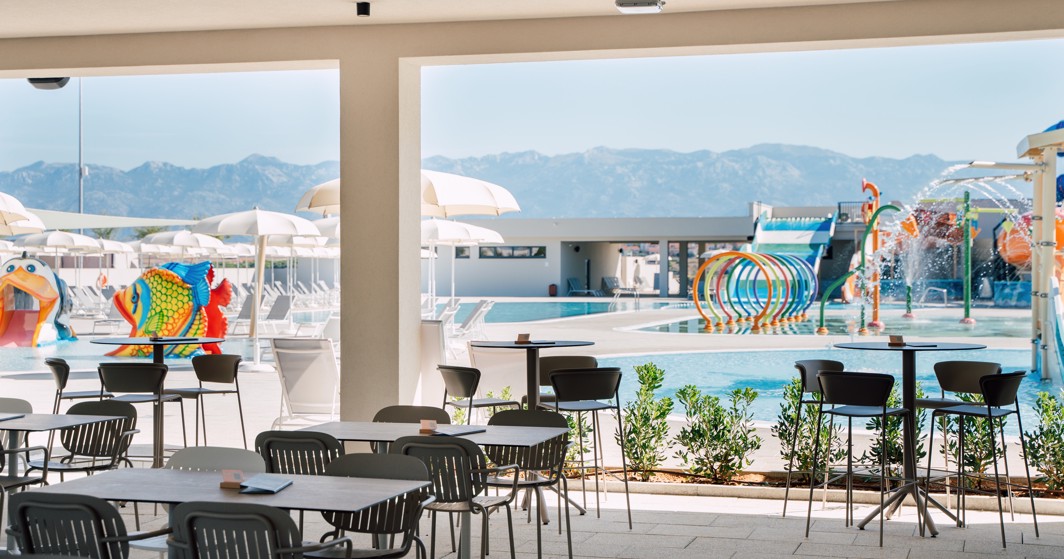 Terrasse von der Bar mit Tischen und Stühlen, Blick auf den Aquapark im Aminess Style Camping Avalona Resort.