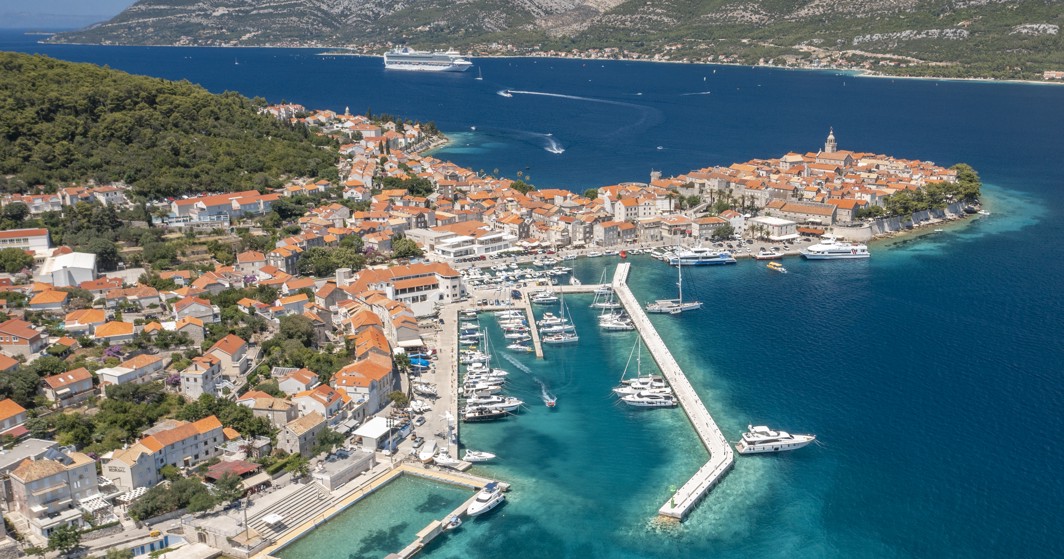 Zapanjujući zračni pogled na grad Korčulu i njegovu obalu, prikazujući tirkizne vode, šarmantnu luku i zgrade s terakota krovovima u blizini Maradiso Marko Polo by Aminess.