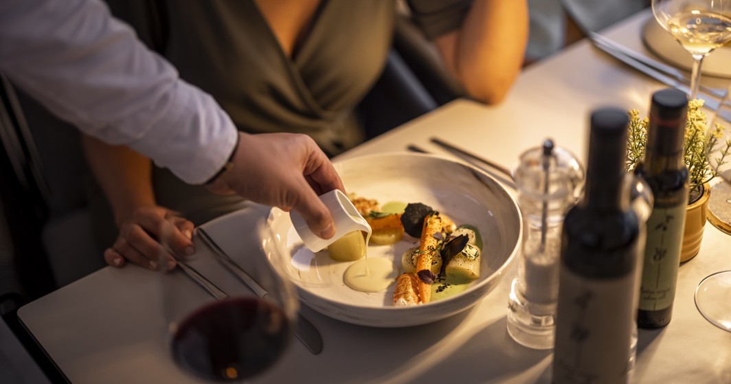 Esperienza di ristorazione elegante al ristorante 7 Seas nell'Aminess Style Camping Atea Resort, con un piatto gourmet servito con bottiglie di vino e bicchieri sul tavolo.