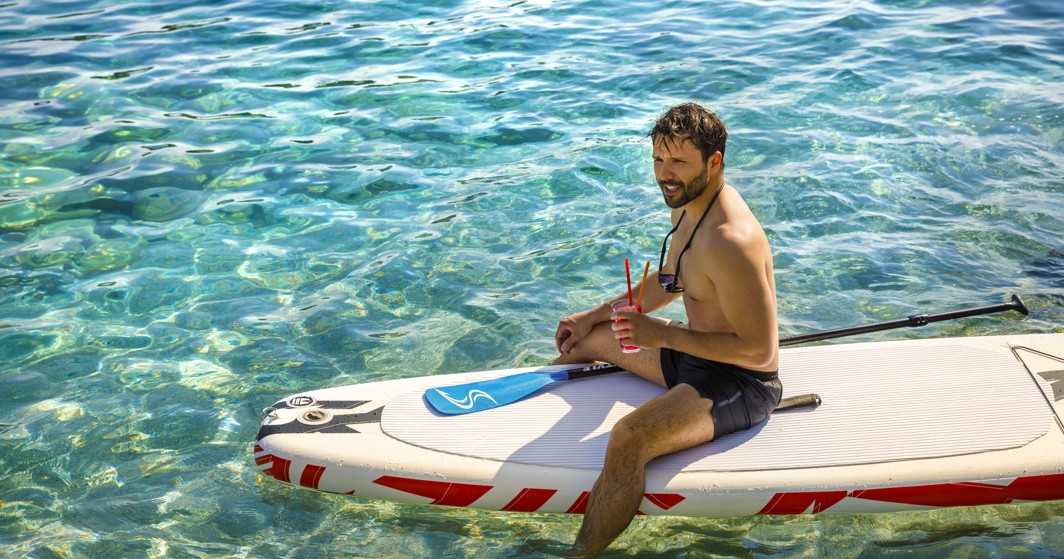 Een man ontspant op een SUP-bord, nippend aan een cocktail.