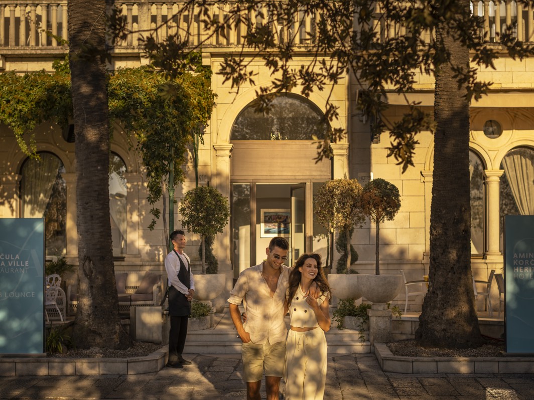 Couple in front of the historic facade of Aminess Korcula Younique Heritage Hotel with lush vegetation shadow