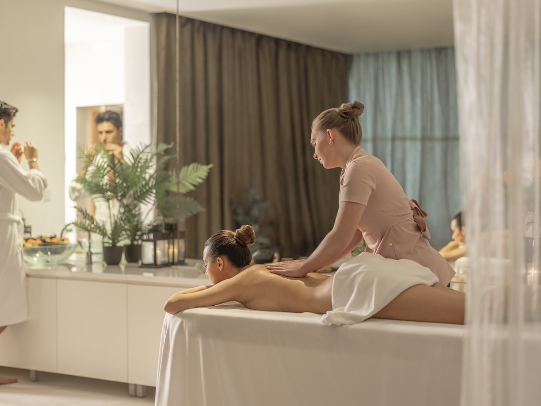 Par v wellness sobi za dva, ženska prejema masažo, medtem ko moški umiva obraz.