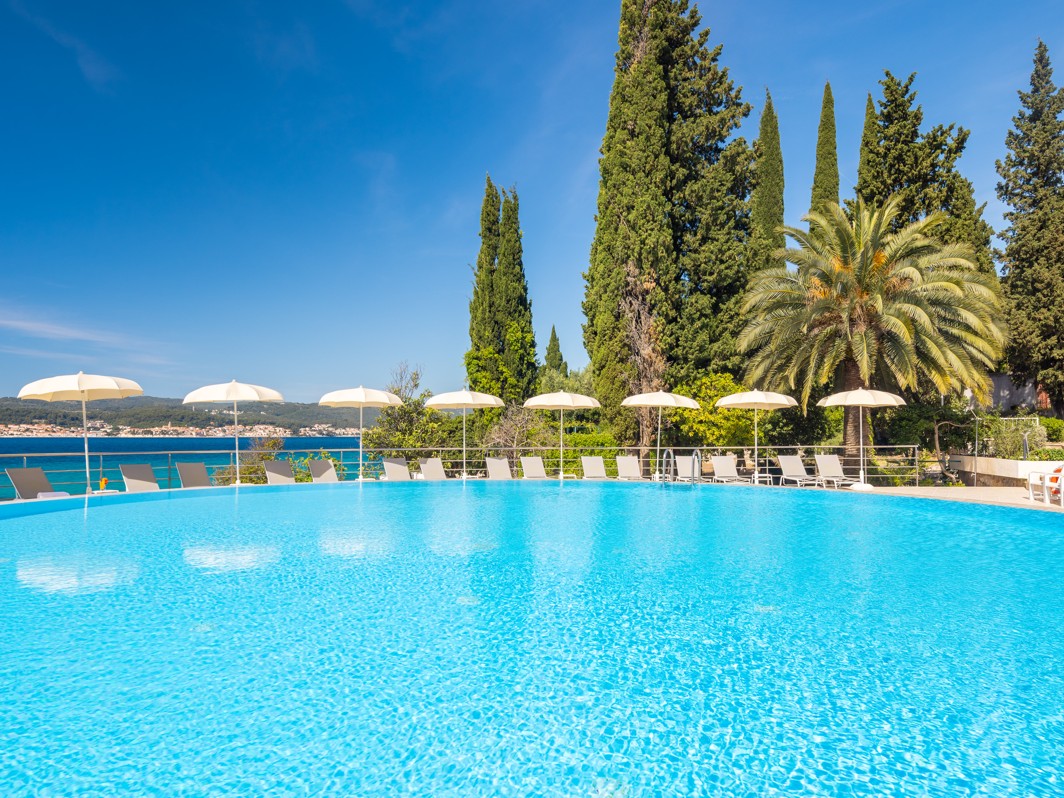 Outdoor pool at Orsan Maradiso Hotel by Aminess with white umbrellas and greenery.