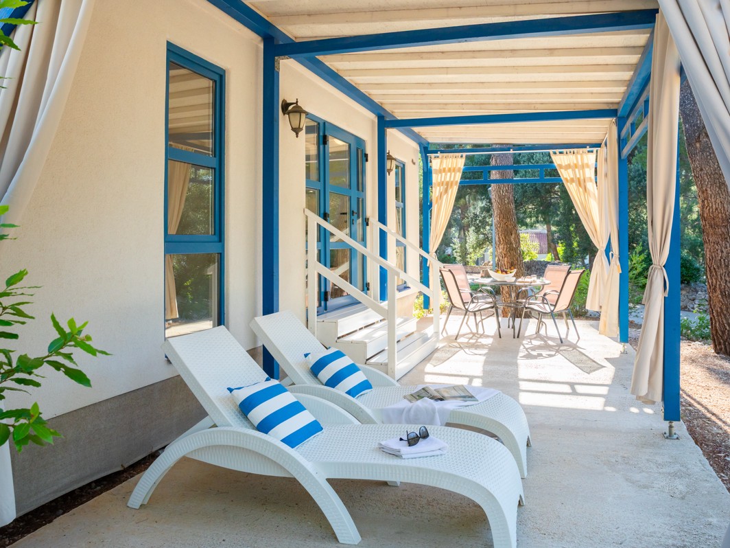 Terasa ispred Marko Polo Holiday Home u Port9 Planet Camping by Aminess, Korčula, sa strukturama uokvirenim plavim bojama okruženim borovima pod vedrim nebom.
