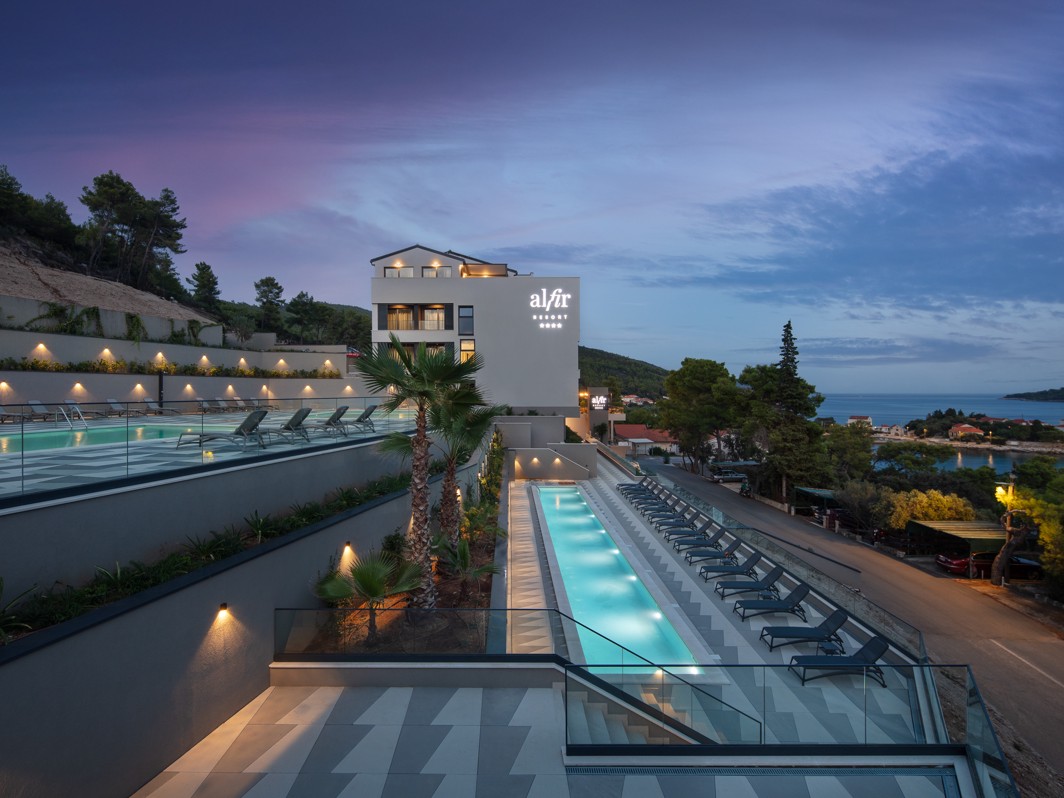 Osvetljeni zunanji bazeni v Aminess Alfir Resortu z ležalniki in pogledom na morje v elegantnem večernem ambientu