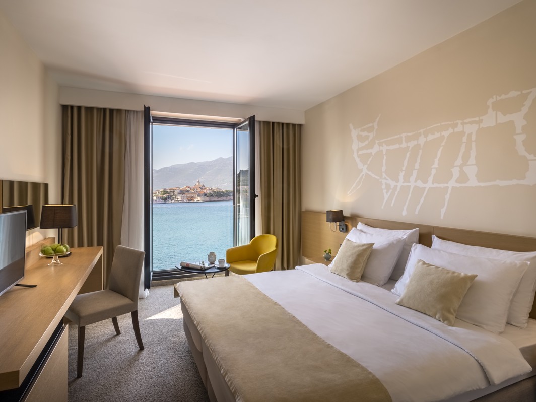 Modern minimal seaside room featuring window view over the old town of Korcula in Croatia at Aminess Younique Liburna Hotel.