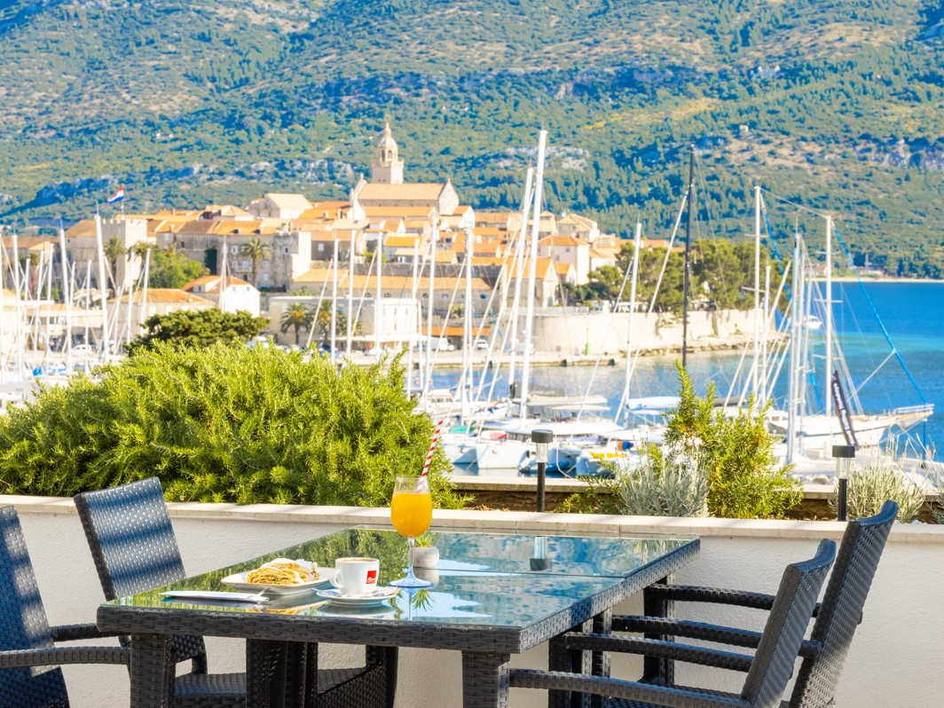 Bar uz bazen u Maradiso Marko Polo by Aminess u Korčuli s povišenim pogledom na marinu, zgrade grada s crvenim krovovima i bujno zelenilo.