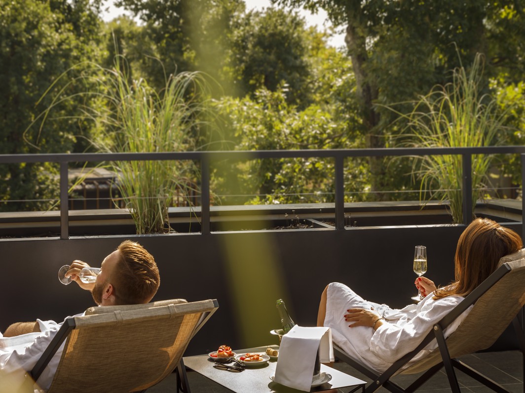 Par se opušta na terasi u ležaljkama, uživajući u pićima s pogledom na bujno zelenilo u pozadini.