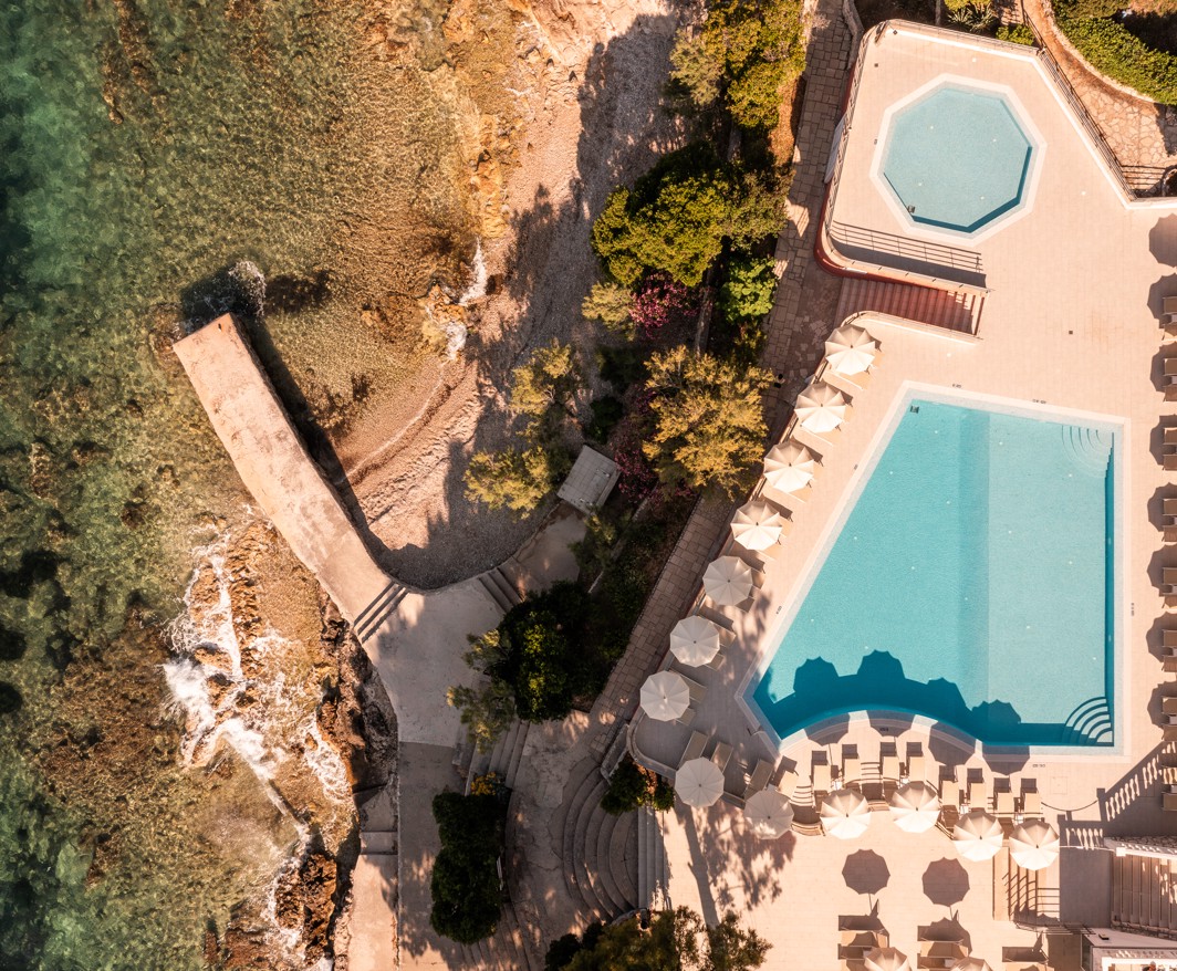 Pogled iz ptičje perspektive na Aminess Younique Bellevue Hotel smješten među bujnim zelenilom, s privatnom plažom i izravnim pristupom moru.