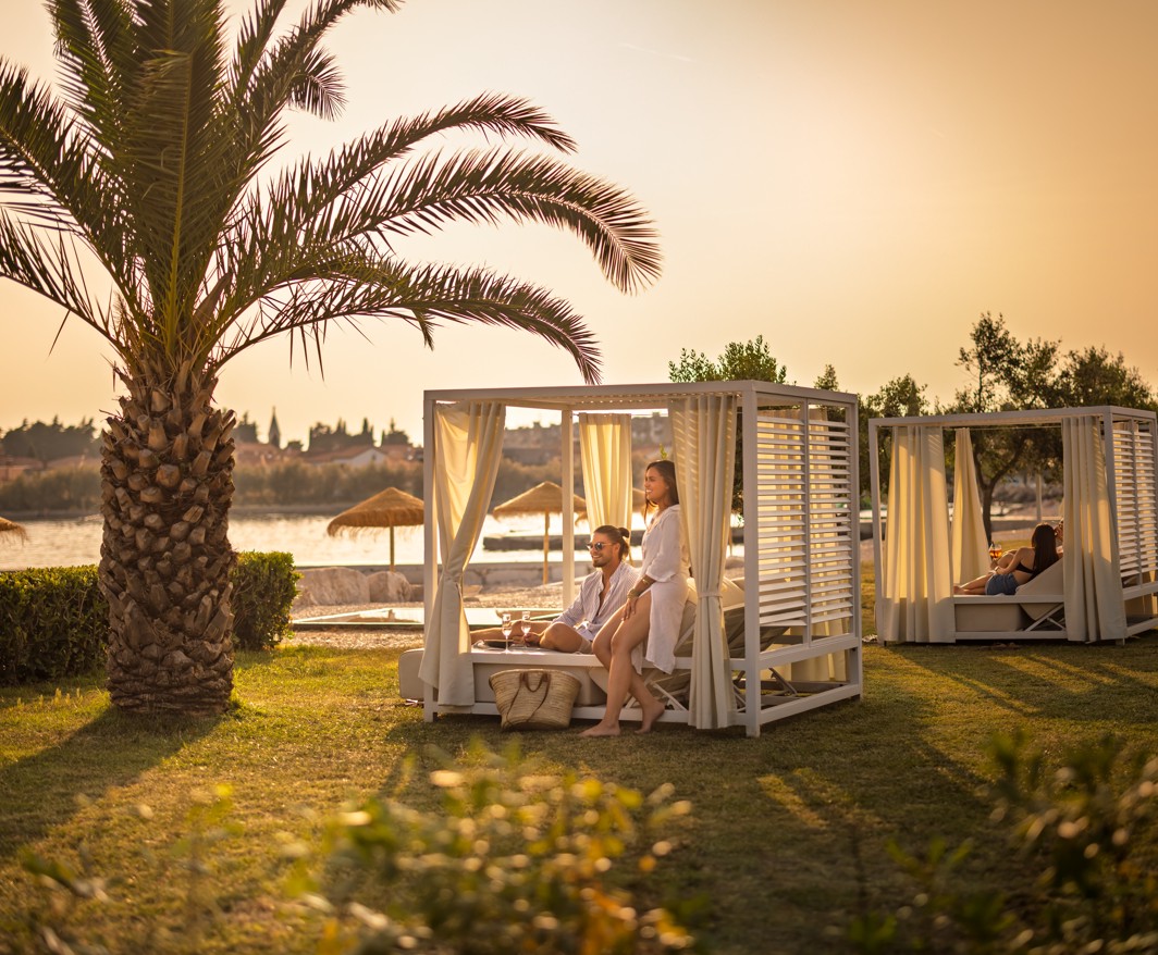 Ospite che si rilassa in una cabana privata circondata da palme presso il bar Aminess a Novigrad, Istria.