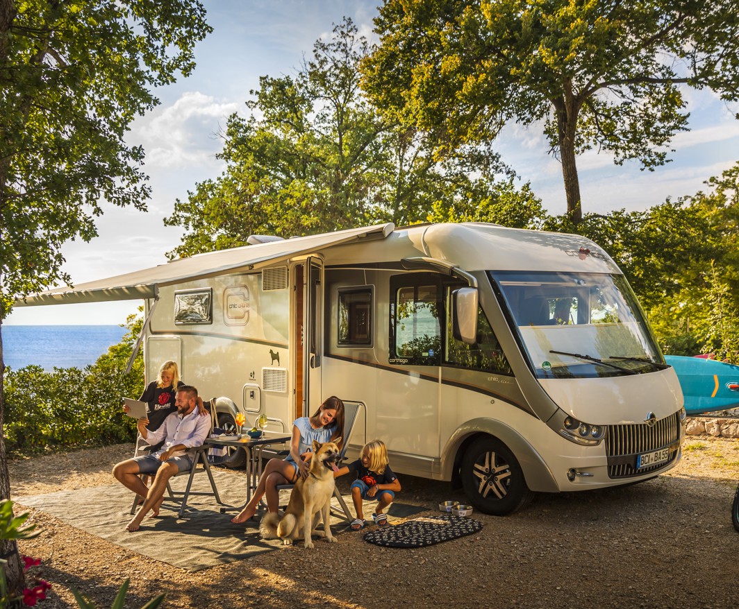 Family camping at Aminess Style Camping Atea Resort, featuring a camper surrounded by trees.