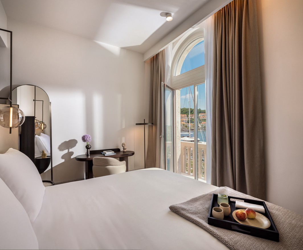 Modern Aminess hotel room with breakfast on the bed and a marina view.