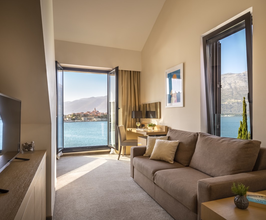 Una moderna e sofisticata camera superiore con una grande finestra che offre una vista mozzafiato sul mare e sulla vecchia città di Korcula presso l'Aminess Younique Liburna Hotel.