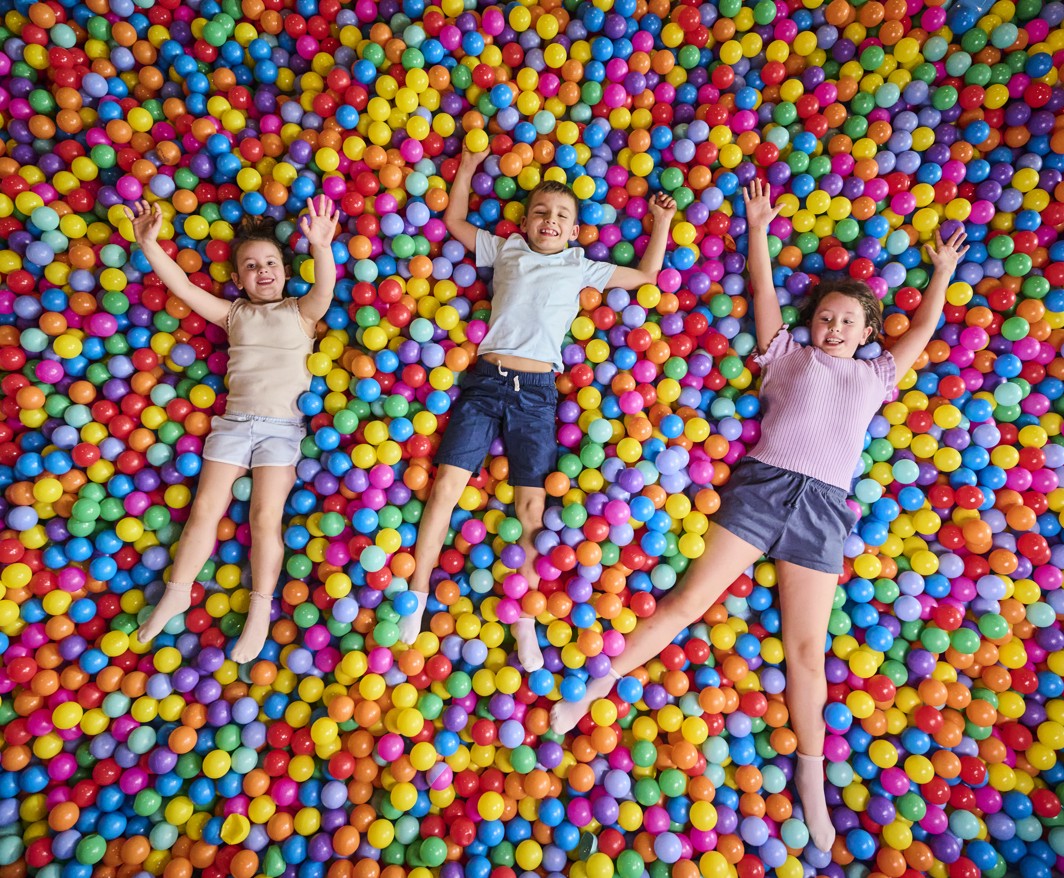 Children play and lie in a colorful ball pit in a kids indoor play area