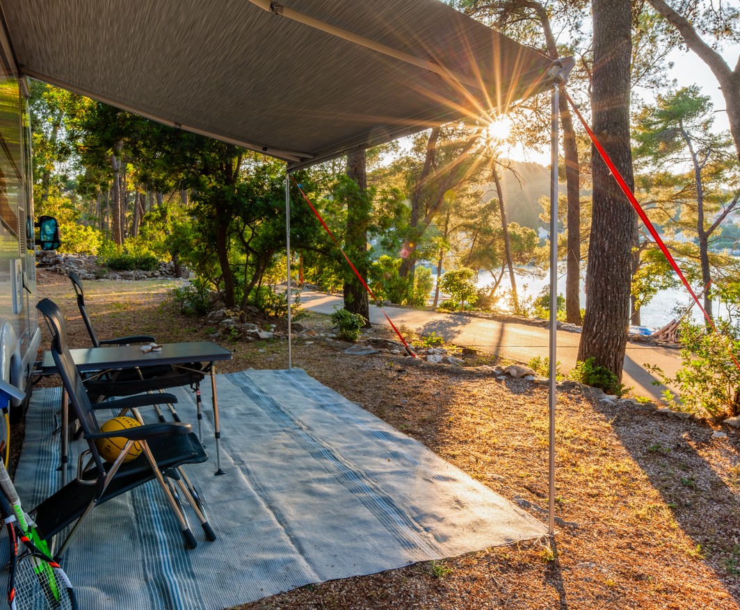 Ein gemütlicher Campingplatz bei Aminess Port9 Planet Camping Korcula mit einem Wohnmobil, beschattet von Bäumen und bietet eine ruhige Atmosphäre unter dem goldenen Schein der Sonne.