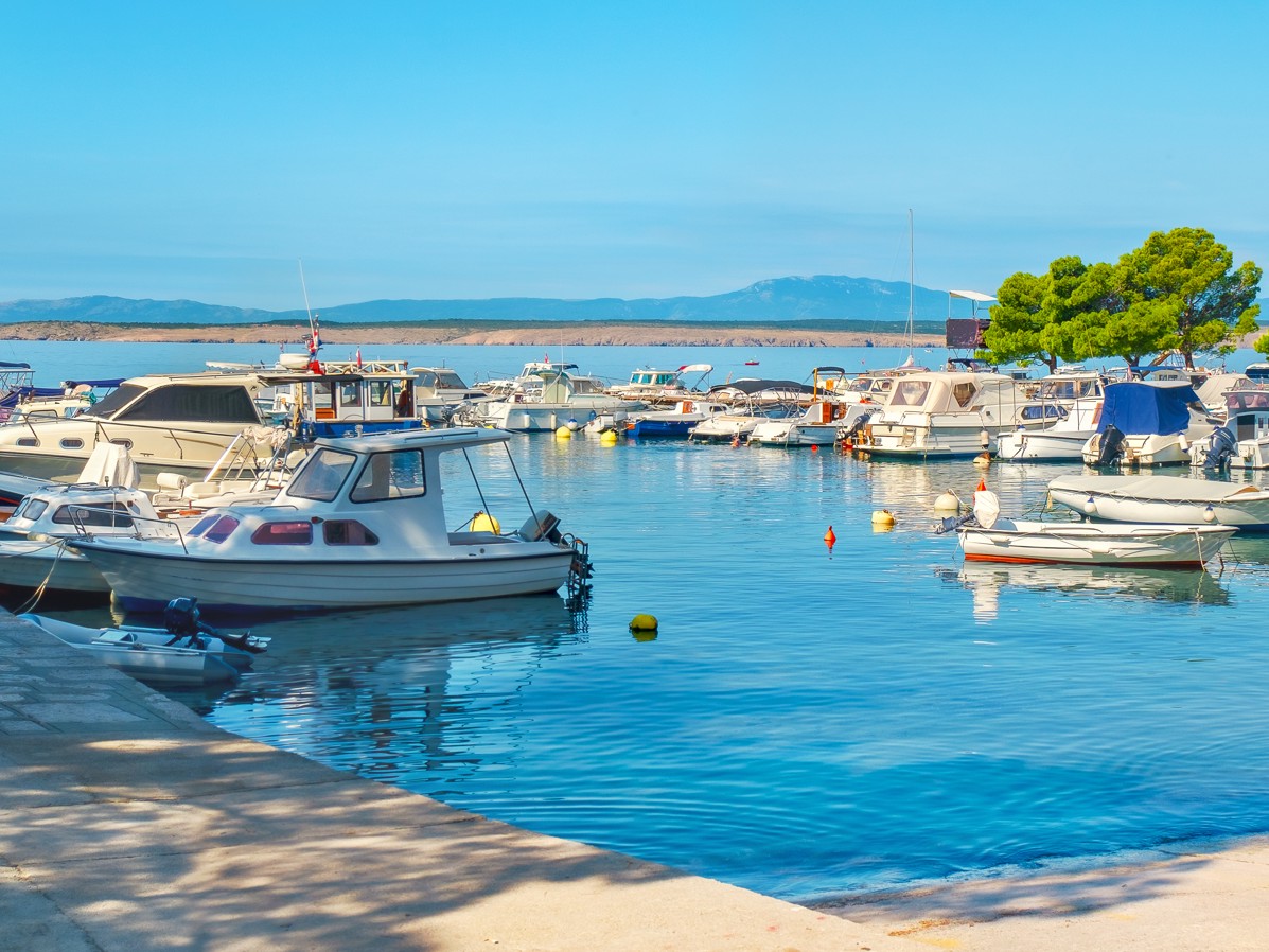Marina with boats docked along a calm beachfront under clear skies in Crikvenica.