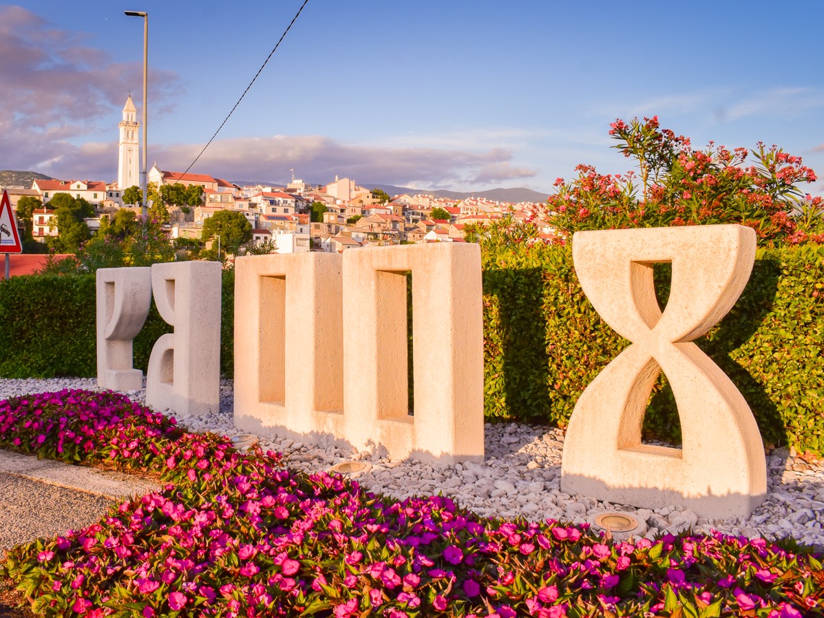 Glagolitic script monument in Novi Vinodolski, Croatia, surrounded by flowers and scenic town view.
