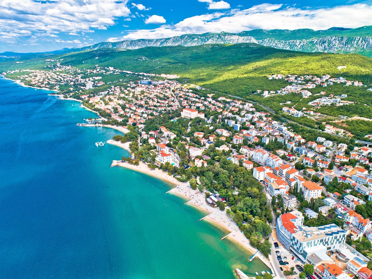 Aerial view of the coastline in Crikvenica, Croatia, with turquoise waters and green hills.