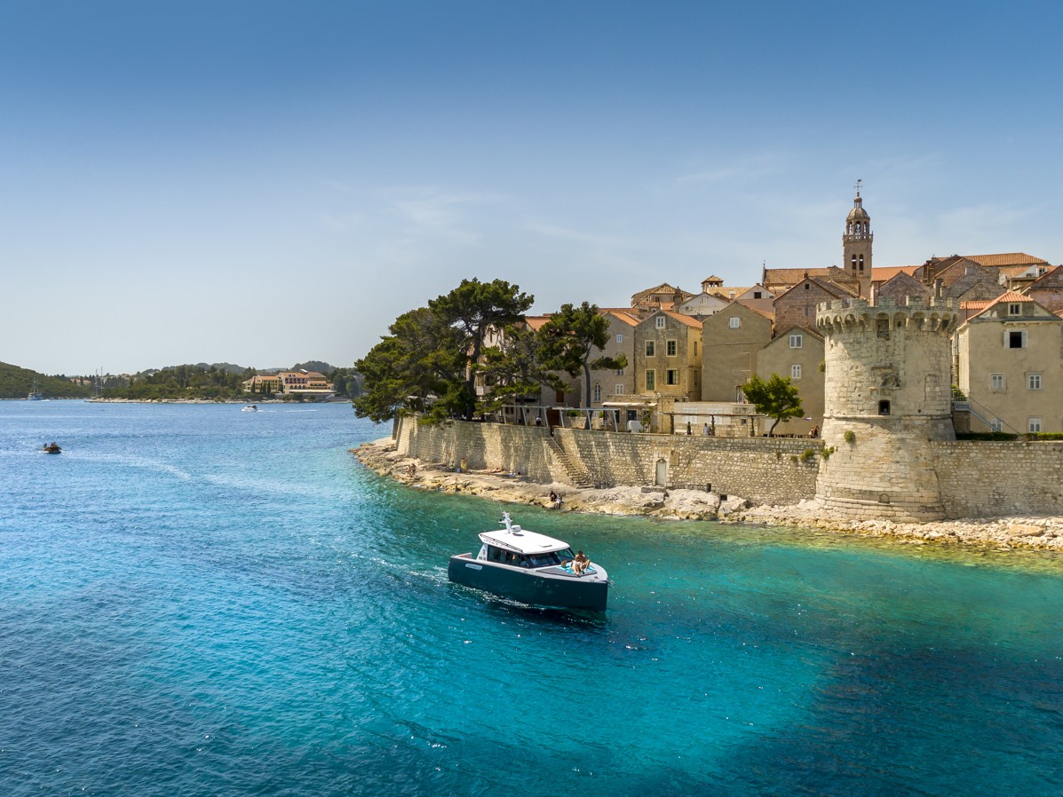 Scenski pogled na Stari grad Korčulu s mora, s srednjovjekovnim kamenim građevinama i brodovima na bistrom Jadranskom moru.