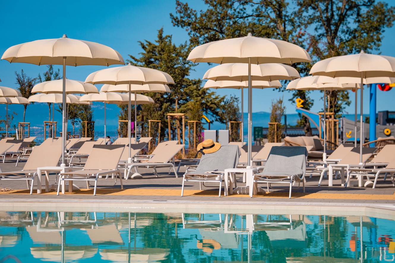 Območje ob bazenu z ležalniki in bež senčniki s pogledom na morje v Aminess Style Camping Atea Resortu.