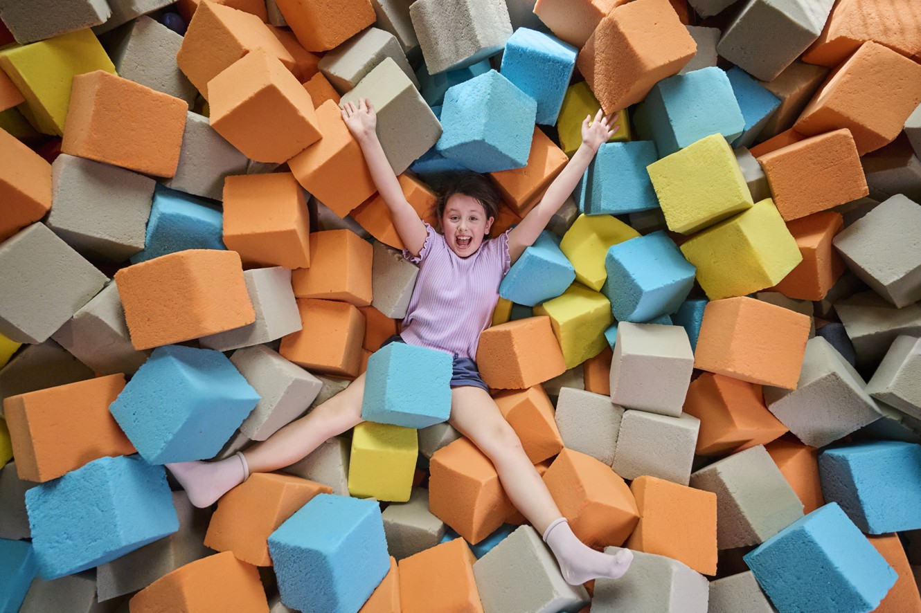 Girl plays and lies in a foam cube pit in a kids indoor play area