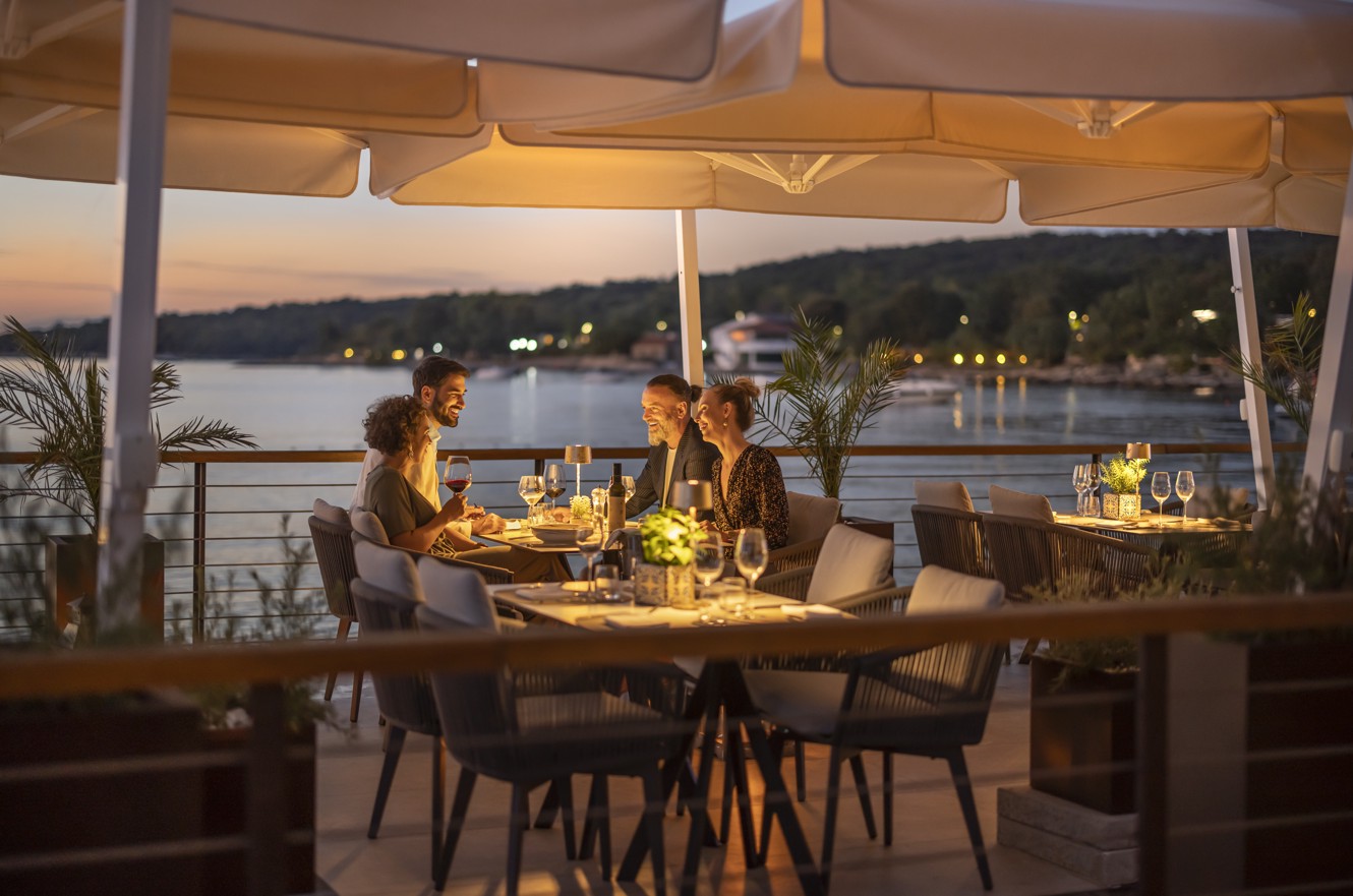 Skupina prijateljev uživa v večerji v restavraciji & baru 7 Seas blizu Aminess Style Camping Atea Resort, s čudovitim pogledom na sončni zahod.