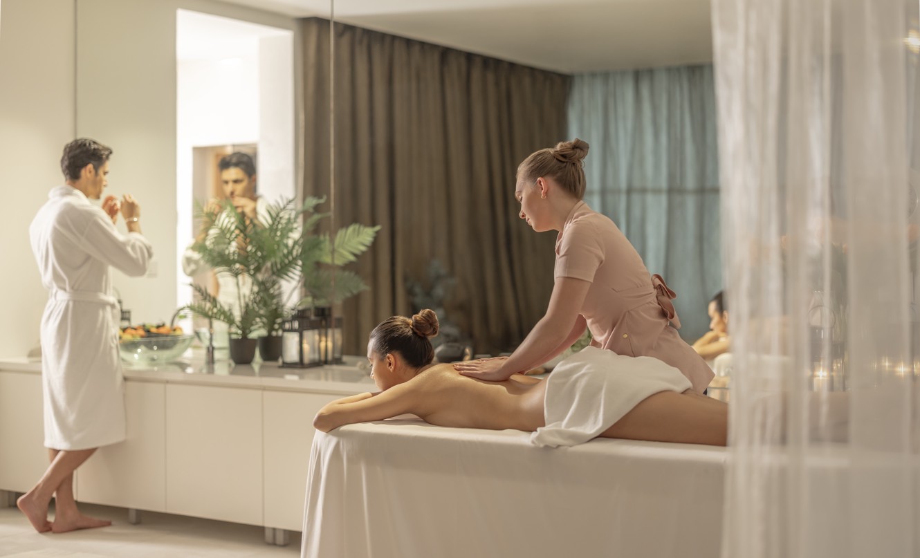 Coppia in una sala benessere per due in un resort, donna che riceve un massaggio mentre l'uomo si lava il viso.