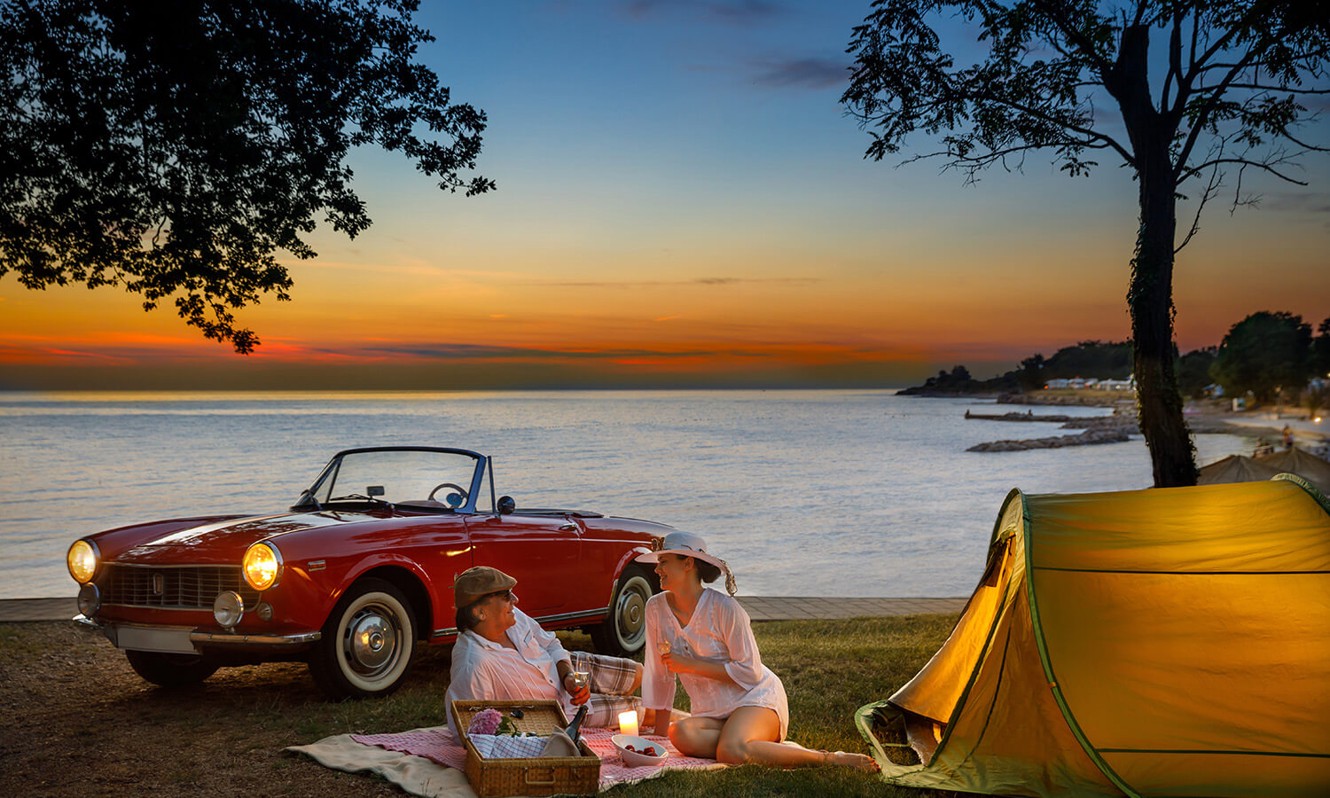 Couple camping at Aminess Planet Camping Maravea, Novigrad, with a vintage car and the sunset in the background