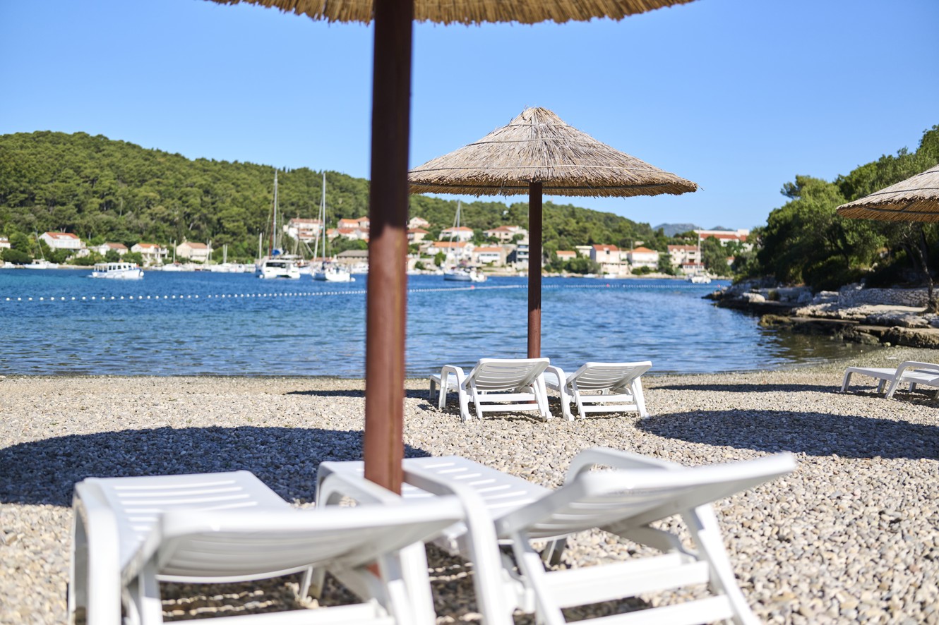 Ein entspannender Kieselstrand in der Nähe von Aminess Port9 Planet Camping Korcula, mit Sonnenliegen und Strohschirmen vor dem Hintergrund des klaren blauen Meeres