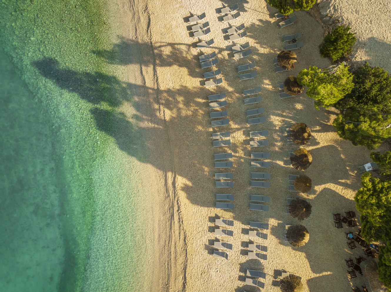 Der Strand vor dem Hotel mit schön arrangierten Liegestühlen und Sonnenschirmen im Aminess Laurel Khalani Hotel.