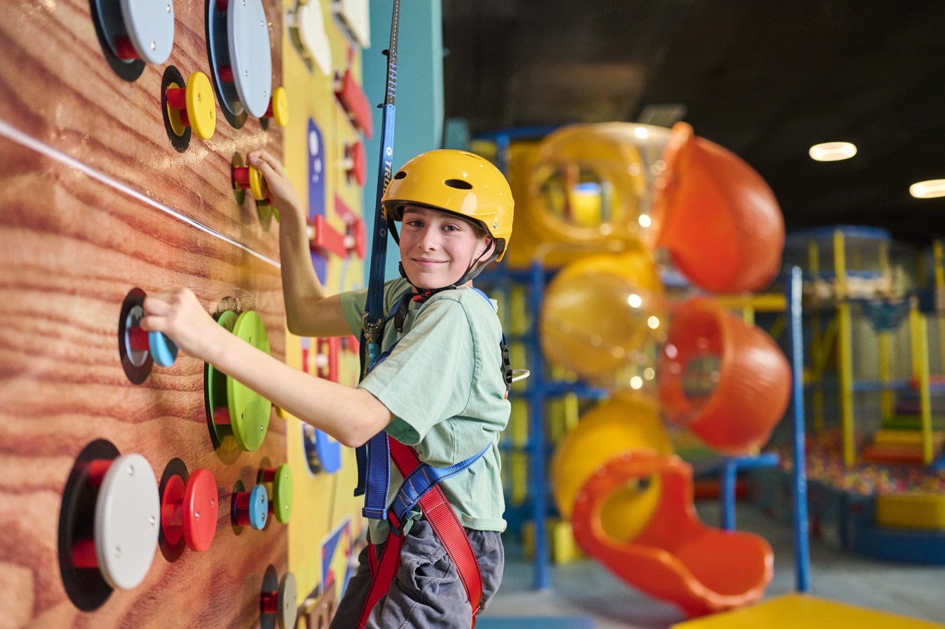 Child wearing a helmet climbs an indoor climbing wall in a kids play area