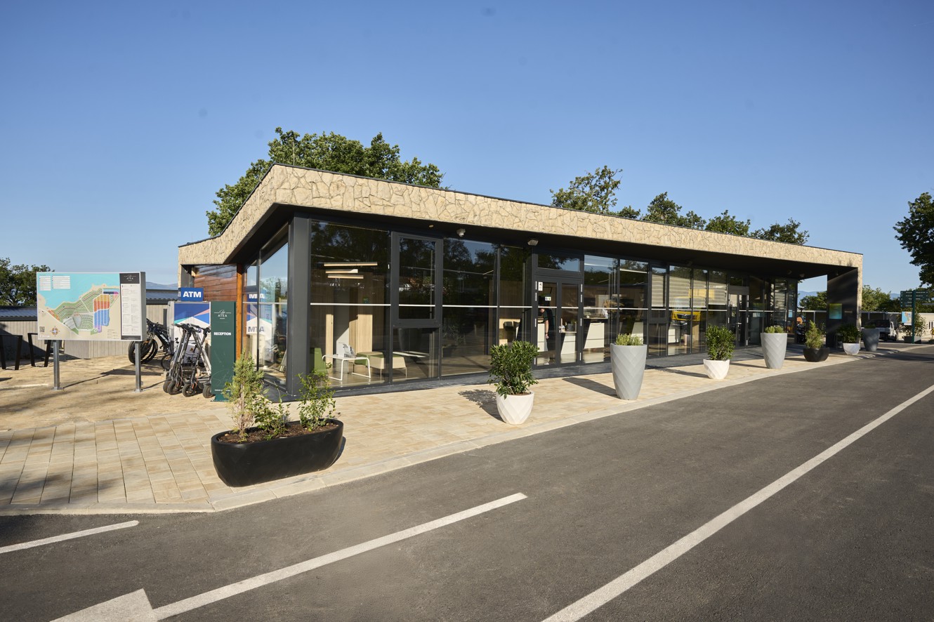 Zunanjost recepcije kampa Aminess Atea na Krku z moderno arhitekturo in velikimi steklenimi stenami.