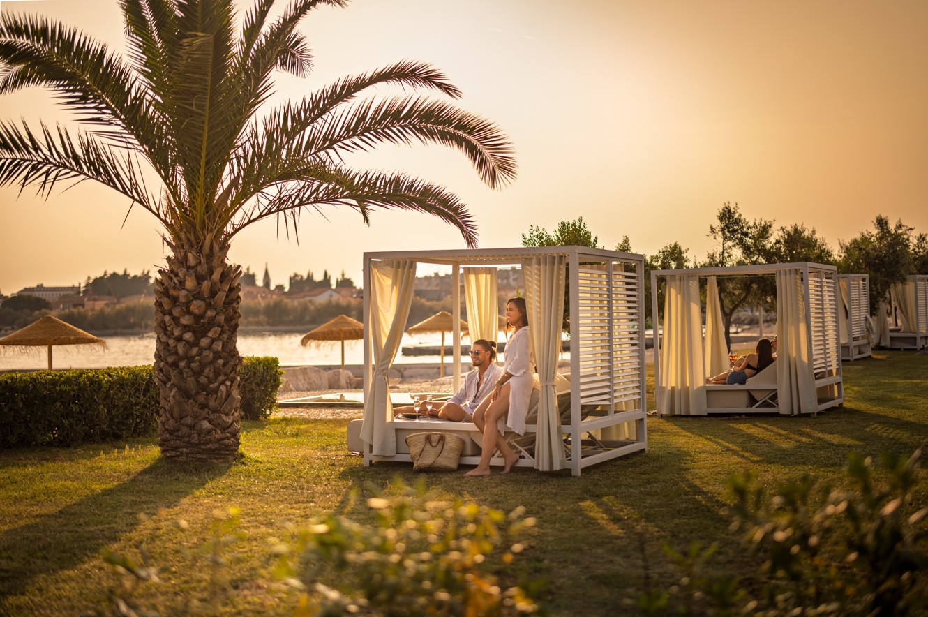 Gost se sprošča v zasebni kabani, obdani s palmami, v baru Aminess v Novigradu, Istra.