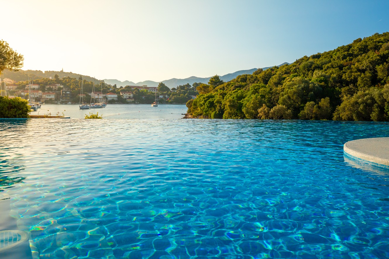 View across the sunlit pool towards the beach in front of the Aminess Vival Port9 Resort.