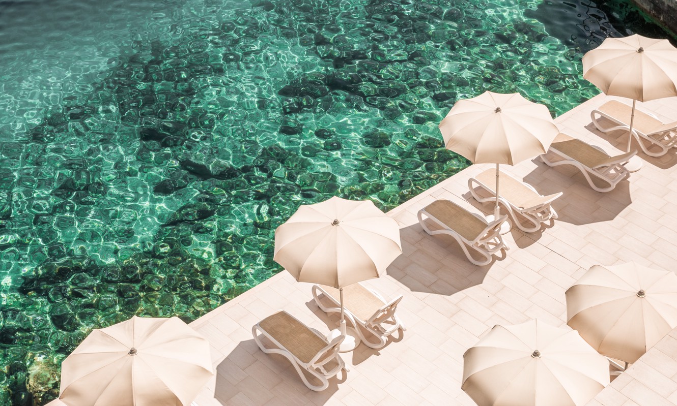 Sun loungers under umbrellas by the turquoise sea in front of Aminess Lume Hotel
