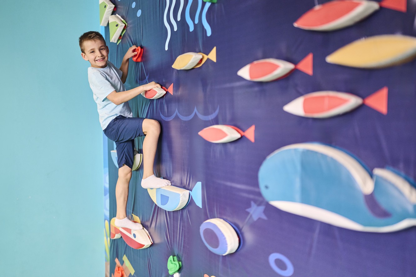Boy climbs an indoor climbing wall with underwater theme in a kids play area