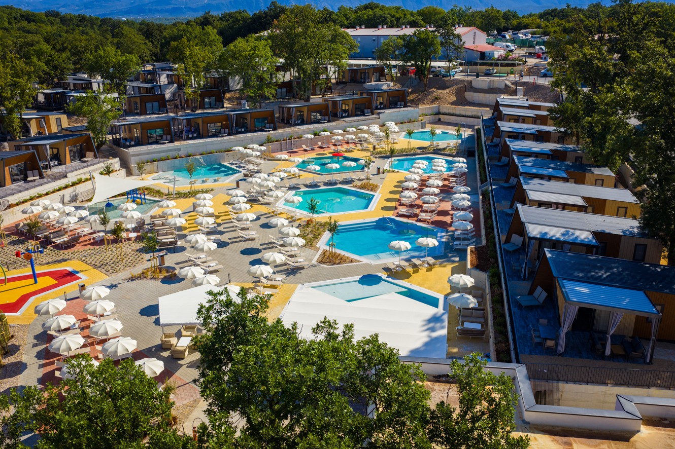 Dvignjen pogled na osrednji bazenski kompleks z ležalniki, senčniki in okoliškimi mobilnimi hiškami v Aminess Style Camping Atea Resortu.