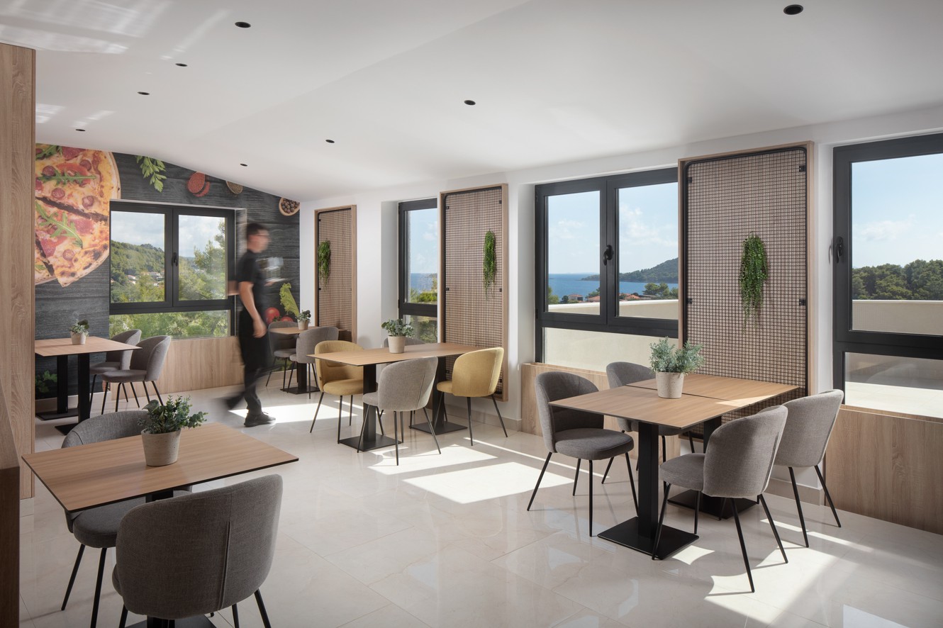 Licht restaurantinterieur in het Aminess Alfir Resort met modern houten meubilair, natuurlijk licht, uitzicht op zee en een warme sfeer